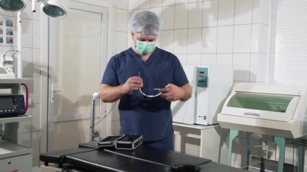 Ιατρικές προμήθειες είναι στα χέρια της ένα γιατρό στην κλινική. Διαγνωστικός εξοπλισμός στην χειρουργική αίθουσα. Ο χειρουργός άνθρωπος προετοιμάζει για τη χειρουργική επέμβαση στο νοσοκομείο, βάζει γυαλιά. Αποστειρωμένο εξοπλισμό και — Αρχείο Βίντεο