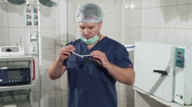 Klinikte doktor elinde tıbbi malzeme vardır. Tanı Cihazları cerrahi odasında. Cerrah adam hastanede ameliyat için hazırlar, gözlük koyar. Steril ekipmanları ve