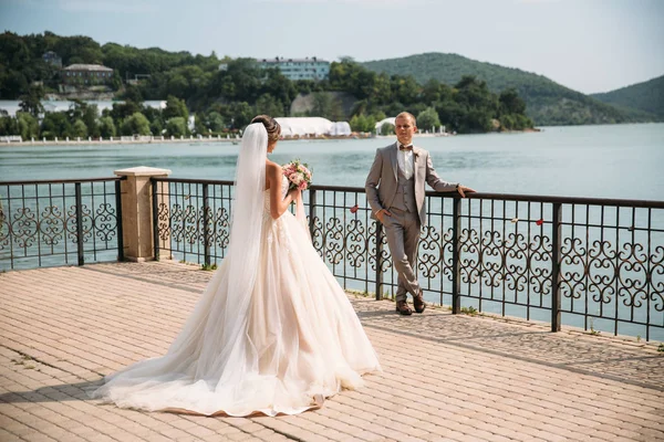 Vackra bröllopsparet, bruden och brudgummen. Söt flicka i lång vit klänning, män i grå kostym. landskap i bakgrunden. Begreppet familj. — Stockfoto