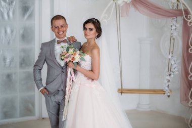 parlak studio sarılma güzel düğün çifti. İş gri damat takım elbise, beyaz bir gömlek bir papyon ve bir ilik, bir gelin duvak ve bir buket çiçek ile lüks elbiseli