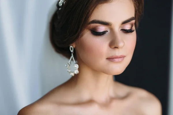 Retrato de cerca de la novia con pendientes de diamantes, maquillaje de boda y poses de peinado en un estudio oscuro. Hermosa joven morena sobre fondo blanco y negro. Concepto de matrimonio, piel clara —  Fotos de Stock