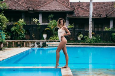 Yakınındaki bir havuz mavi su ile güneşlenme bikinili güzel kız. Seksi model spor şekil ile istirahat ediyor. Hafta sonları bir mayo tatil kıvırcık saçlı genç kadın.