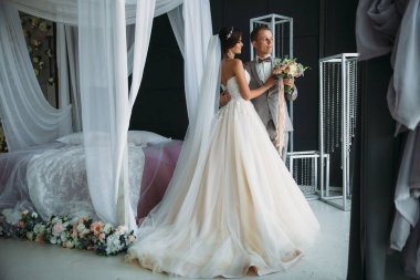 Düğün günü, gelin ve damat parlak studio sarılma. Gri takım elbise, Beyaz gömlekli adam papyon var. Buket çiçek elinde tutan uzun lüks içinde genç güzel kadın.