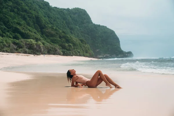Wspaniała młoda dziewczyna w bikini beżowy położony jest przy plaży, opalanie w pobliżu oceanu. Model z sexy ciało i sportowej sylwetki w wodzie czystego morza na wyspie. Pojęcie na weekend — Zdjęcie stockowe