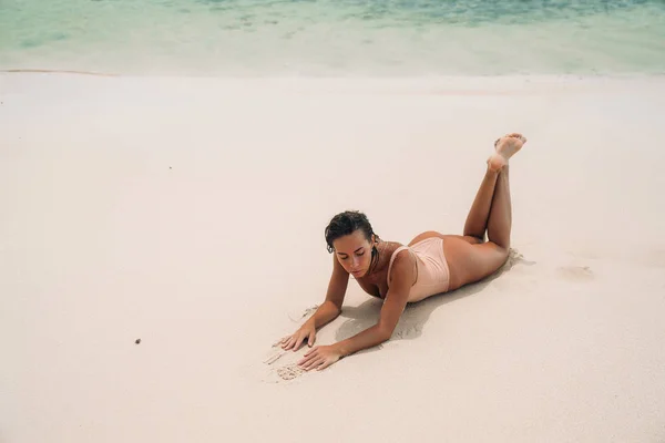 ベージュのビキニでゴージャスな若い女の子は、海の近くに日光浴、ビーチであります。セクシーなボディと島の澄んだ海の水のスポーツ図の模型。週末の概念 — ストック写真