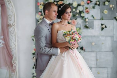 Düğün gününde yeni evliler portresi. Damat ile beyaz bir gömlek ve bir papyon gri elbiseli bir örtü ile lüks beyaz elbise ile güzel bir gelin sarılmak. Kız makyaj ve hairdress ile