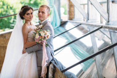 Düğün gününde yeni evliler portresi. Damat ile beyaz bir gömlek ve bir papyon gri elbiseli bir örtü ile lüks beyaz elbise ile güzel bir gelin sarılmak. Kız makyaj ve hairdress ile