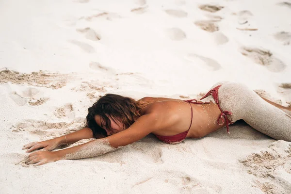 Sexy modelo encontra-se na praia com seu burro na areia. Uma menina bronzeada com uma figura sexy está descansando no mar. Corpo bonito de uma jovem mulher . — Fotografia de Stock