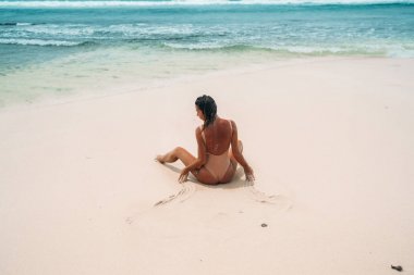 Plaj beyaz kum ile arka görüş güzel bir vücut ile sevimli bir kız. Seksi kadın yaz tatili Okyanusu yakınlarındaki güneş banyosu. Bir kişi ile adanın muhteşem manzara.