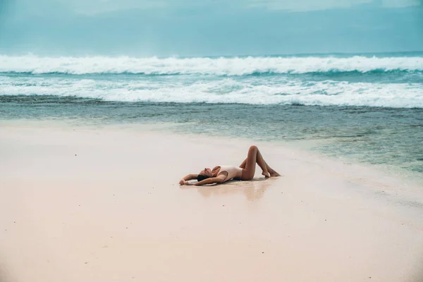 Mooi meisje in een zwembroek ligt aan het strand met wit zand. Sexy model zonnebaden op vakantie in de buurt van de Oceaan. Prachtige landschap van het eiland met een toerist. — Stockfoto