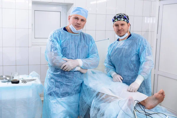 A team of doctors in sterile medical gowns perform surgery in a surgical room. Surgeon with an assistant after the procedures. Portrait of medical workers. — Stock Photo, Image