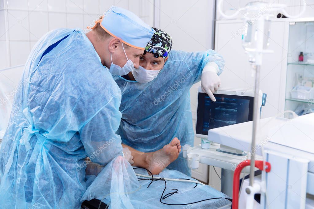 A team of doctors in sterile medical gowns perform surgery in a surgical room. The surgeon shows the diagnostic equipment and communicates with the assistant.