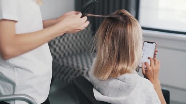 Крупный план рук парикмахеров, наносящих маску на волосы молодой женщины — стоковое видео