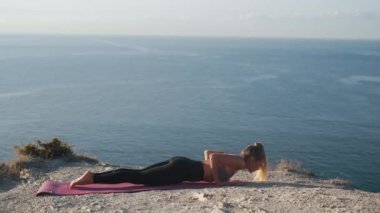 Dağın tepesinde yoga egzersizi yapan kadın, arka planda deniz, yavaş çekim