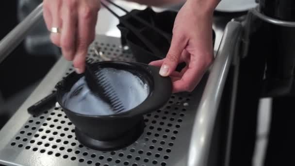 El primer plano de las manos de peluquero mezcla el tinte para el cabello en un tazón de plástico en un salón de belleza — Vídeo de stock