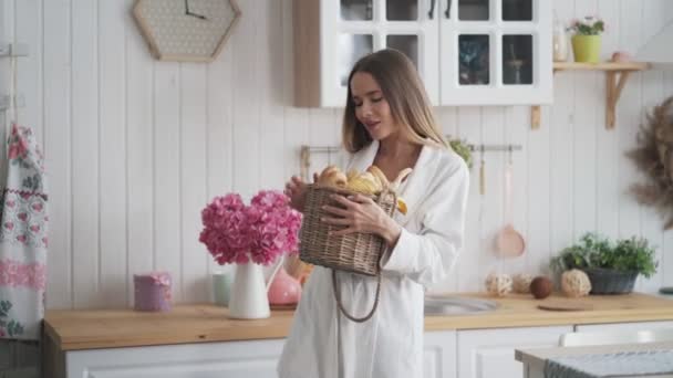 Jeune femme en peignoir aux danses de cuisine avec panier de pain frais — Video