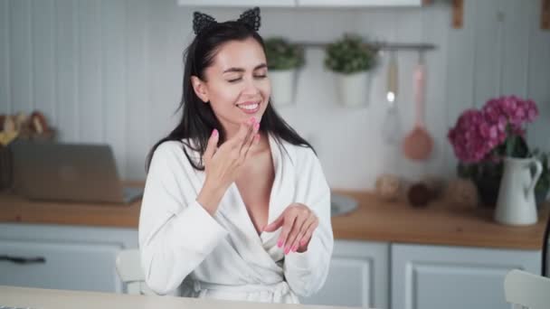 Portrait de femme en peignoir applique de la crème sur son visage et fait un massage facial — Video