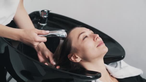 Kuaförün eli kapalıyken kuaförde genç bir kadına saç yıkıyor. — Stok video