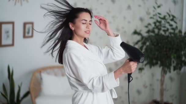 Jonge vrouw in witte badjas danst en droogt haar met haardroger — Stockvideo