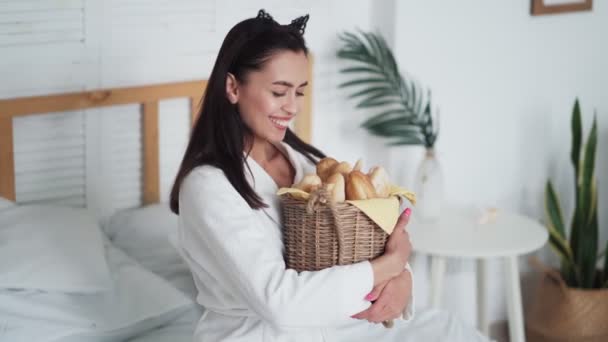 Mujer joven en albornoz blanco sostiene canasta de pan en sus manos y sonríe — Vídeo de stock