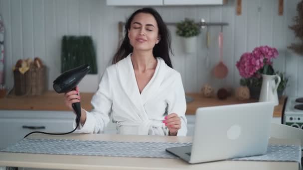 Jonge vrouw in witte badjas droogt haar haar met haardroger, bereidt voor video oproep — Stockvideo