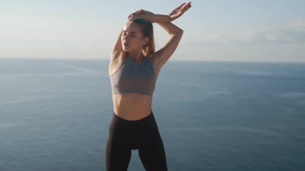 Женщина делает упражнения и растяжки утром, море на заднем плане, замедленная съемка — стоковое видео