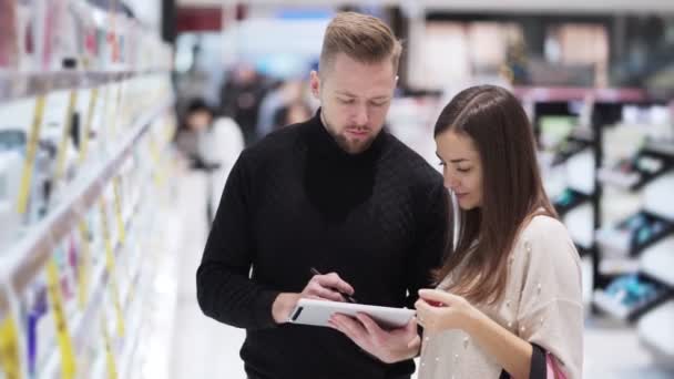 Jonge man en vrouw in cosmetica winkel kijken naar digitale tablet en praten — Stockvideo