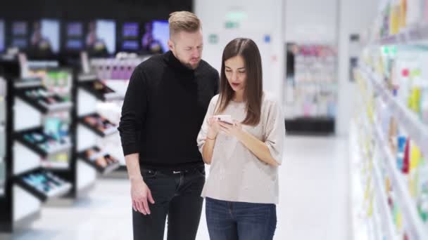 Marido e esposa em loja de cosméticos olhar para smartphone e falar — Vídeo de Stock