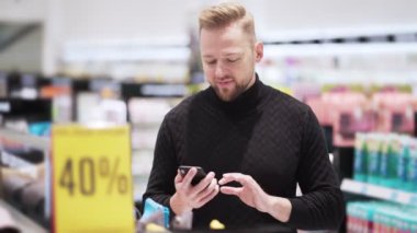 Genç sakallı adamın portresi akıllı telefon kullanıyor ve alışveriş merkezinde mesaj yazıyor.