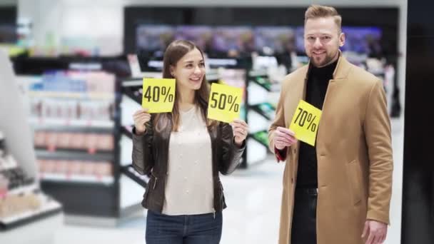 Young woman and man at cosmetics store show discount sign with big sale — Stock Video