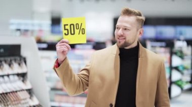 Kozmetik mağazasındaki genç sakallı adam baş parmağını kaldırdı ve indirim tabelasını gösterdi.