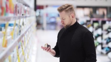 Genç yakışıklı adam ürünleri kozmetik mağazasından seçiyor, alışveriş konsepti.