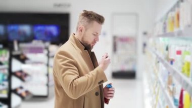 Kahverengi ceketli genç yakışıklı kozmetik mağazasından ürün seçiyor, alışveriş konsepti.