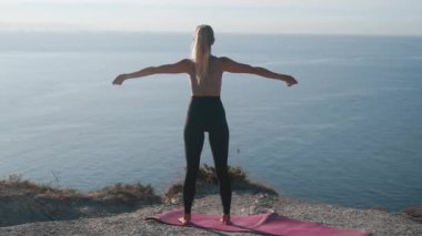 Kadın egzersizler yapar ve sabah uzanır, arka planda deniz, yavaş hareket