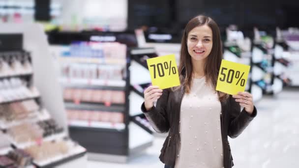 Kvinna på kosmetika butik visar två rabatt tecken, stor försäljning, hon chockade — Stockvideo