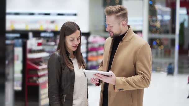 Joven hombre y mujer en la tienda de cosméticos mirar tableta digital y hablar — Vídeos de Stock