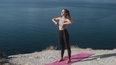 Kadın açık havada lastik bantlar ile egzersiz yapar, vücudunu trenler, yavaş hareket