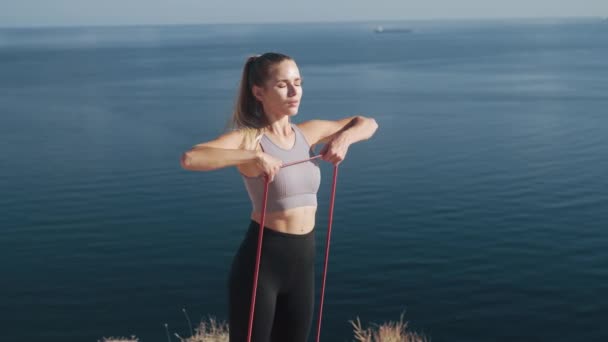 Женщина делает тренировки с резиновыми лентами на открытом воздухе, тренирует свое тело, замедленное движение — стоковое видео