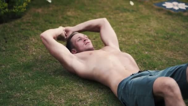 Muscular man doing exercises for abs muscles outdoor — Stockvideo