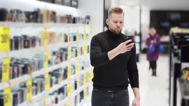 Ung man använder telefonen och tar foto av varor och handelshyllor i butiken — Stockvideo