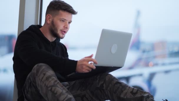 Hombre sentado en el aeropuerto y utiliza el ordenador portátil para el trabajo, avión borroso en el fondo — Vídeos de Stock