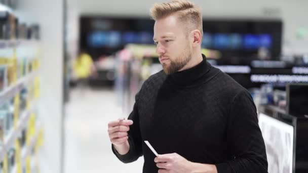 De mens kiest parfum in de cosmeticawinkel, neemt goederen van de plank en snuift eraan. — Stockvideo