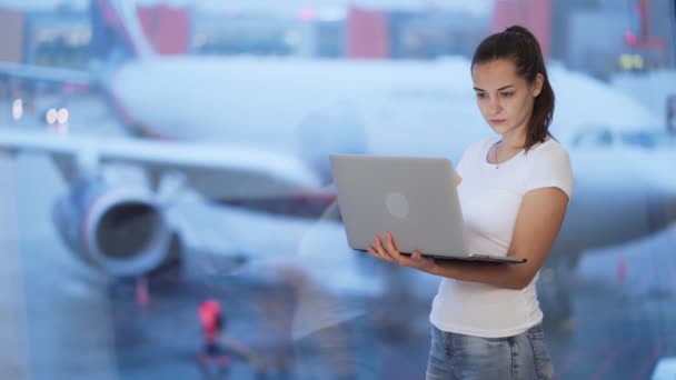 Vrouw werkzaam op computer in de buurt van venster op de luchthaven, wazig vliegtuig op de achtergrond — Stockvideo