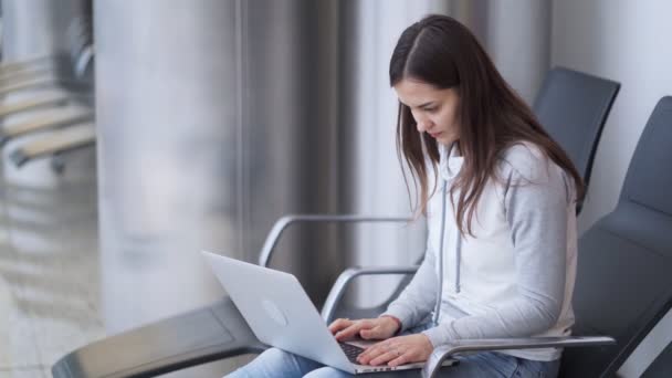 Junge Frau sitzt in Abflughalle und nutzt Laptop für Arbeit am Flughafen — Stockvideo