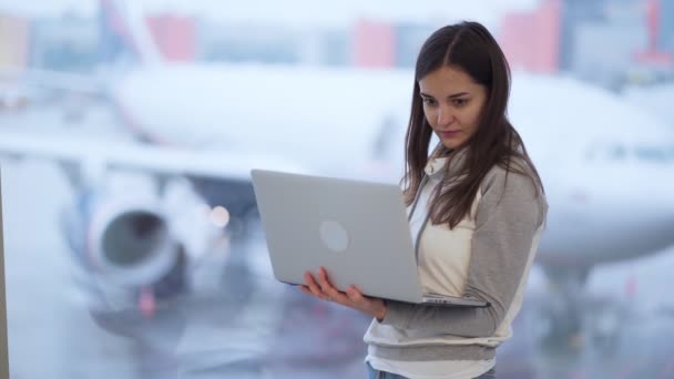 Frau arbeitet am Computer in der Nähe des Fensters am Flughafen, verschwommenes Flugzeug im Hintergrund — Stockvideo