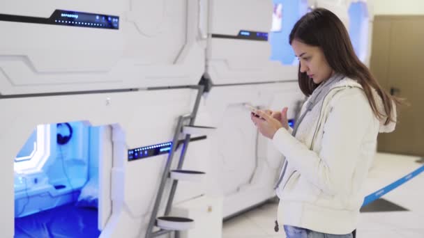 Молодая женщина использует телефон, чтобы оплатить онлайн для сна капсулы в аэропорту — стоковое видео