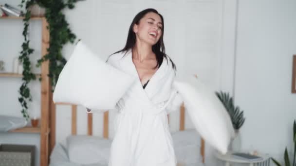 Молодая женщина прыгает в спальню и танцует с подушками дома, смешное видео — стоковое видео