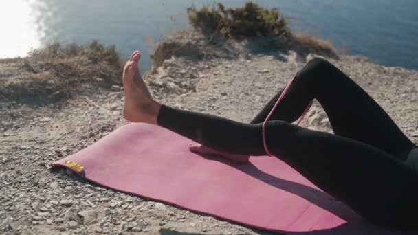 Close-up meisje benen op mat, ze doet oefeningen met elastiekjes, treinen billen — Stockvideo