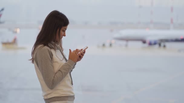 Frau benutzt Handy für die Arbeit am Flughafen, verschwommenes Flugzeug im Hintergrund — Stockvideo