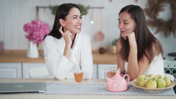 Dos mujeres hermosas beben té en la cocina por la mañana y hablan, hora del desayuno — Vídeos de Stock